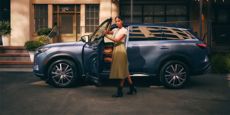 A woman exiting the driver's side of a light blue 2025 INFINITI QX60 that is parked outside a building